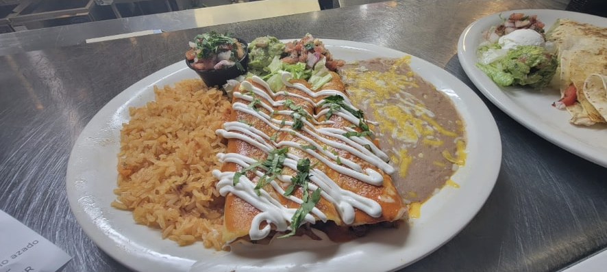 Enchiladas Rojas topped with red sauce, served with Mexican rice, refried beans and guacamole